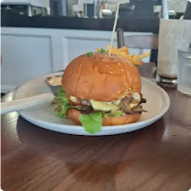 A tall burger in a glossy bun on a white plate
