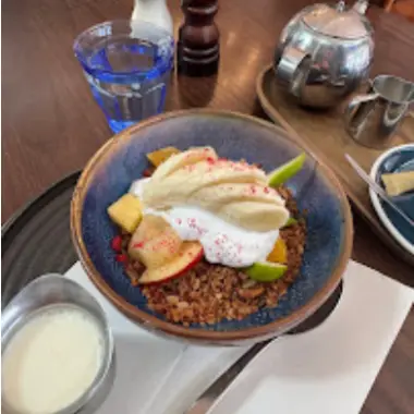 A bowl of granola with yoghurt and fresh apple, with a jug of milk