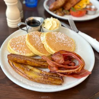 A stack of pancakes with crispy bacon, banana and blueberries