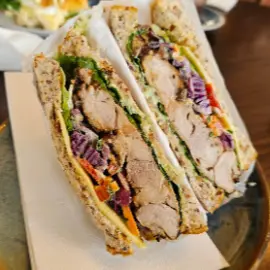 A thick grain-bread sandwich cut in half, filled with chicken and slaw